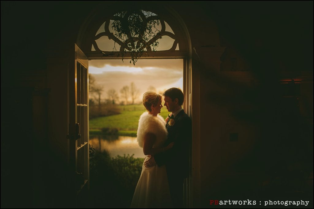 Delbury Hall Wedding Photographer captures a stunning moment of a bride and groom standing in a doorway at sunset.