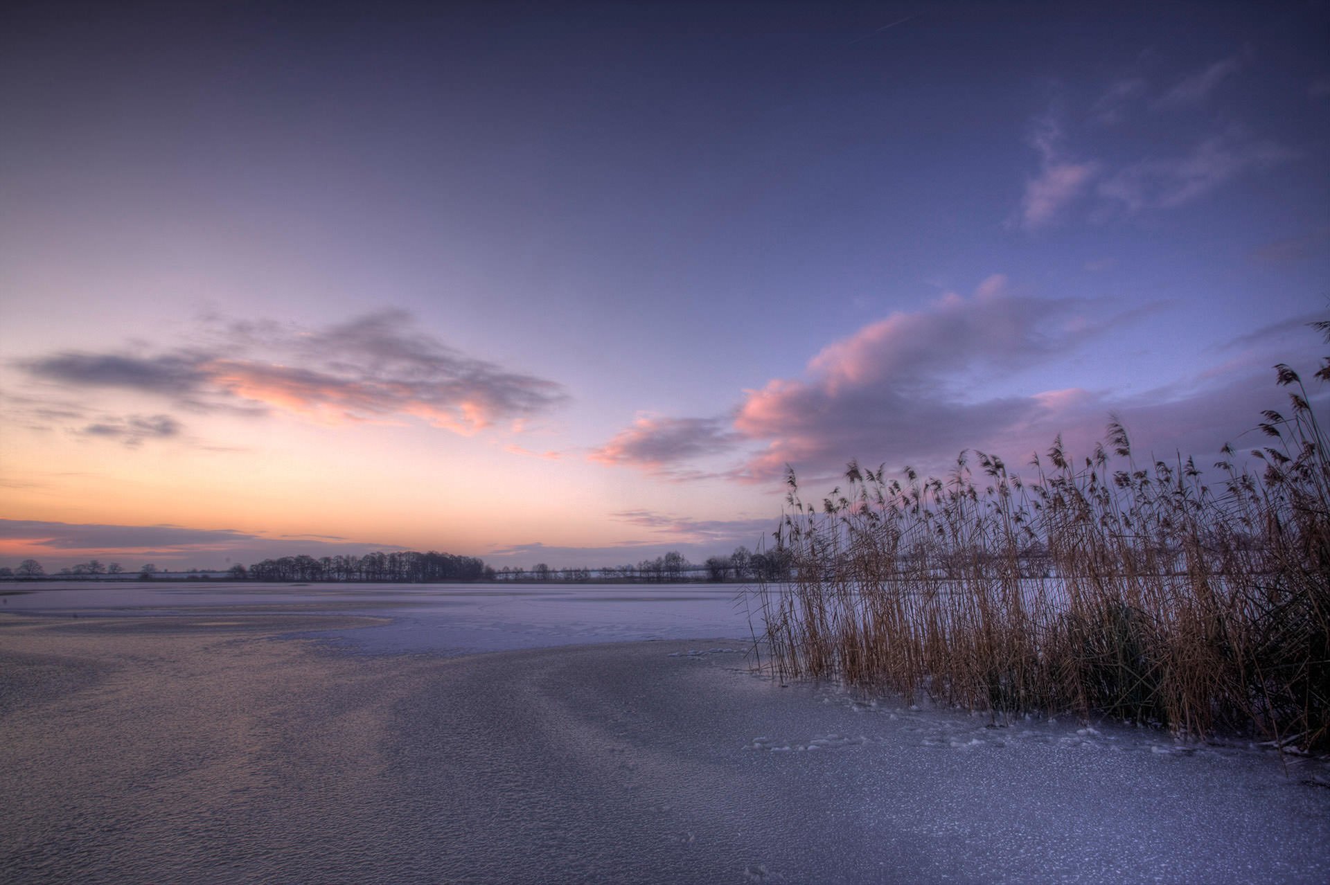 A frozen landscape with a sunset over a lake.