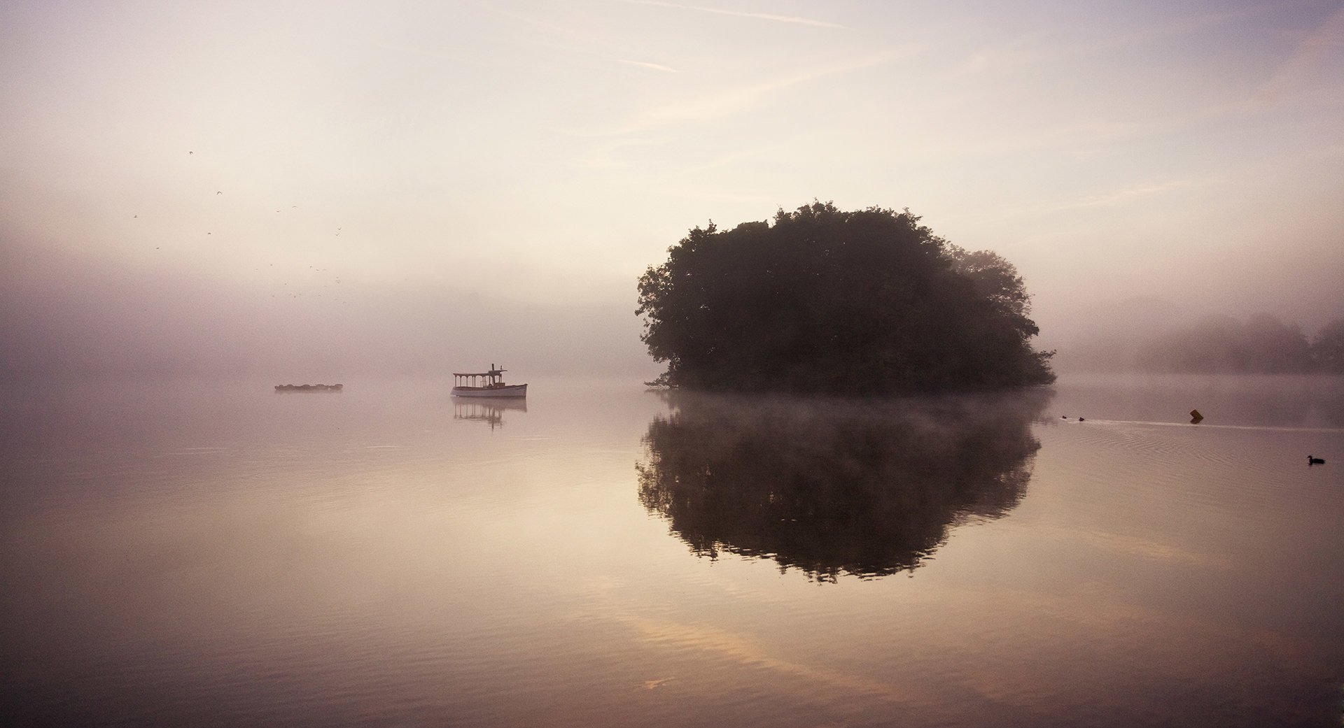 A foggy landscape featuring a boat on a serene lake with a small island.