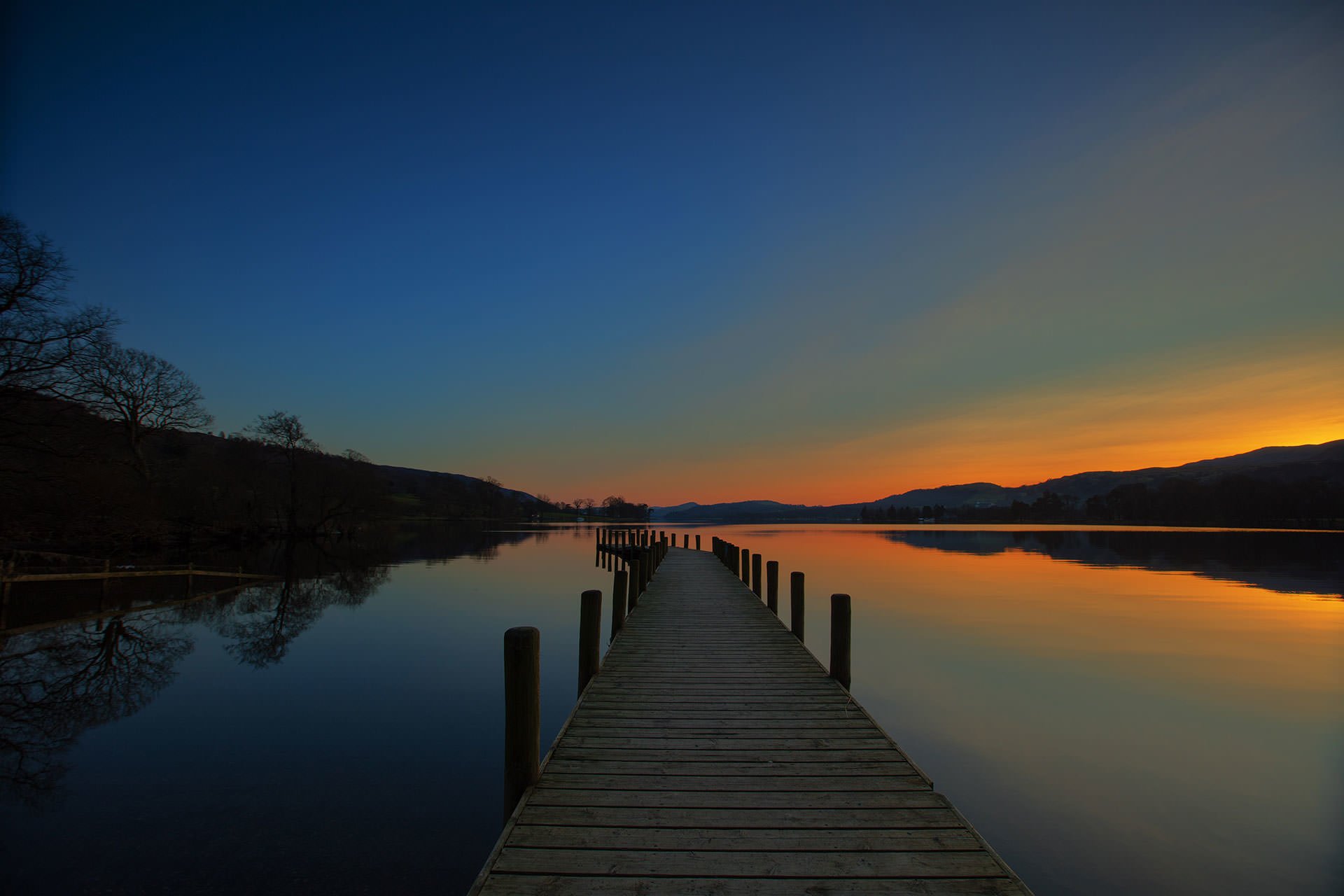 A picturesque landscape featuring a pier on a serene lake bathed in the warm hues of a stunning sunset.
