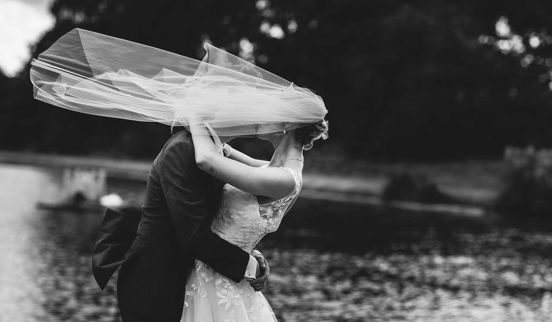 A Shropshire bride and groom share a tender kiss in front of a breathtaking lake, captured by a talented documentary wedding photographer.