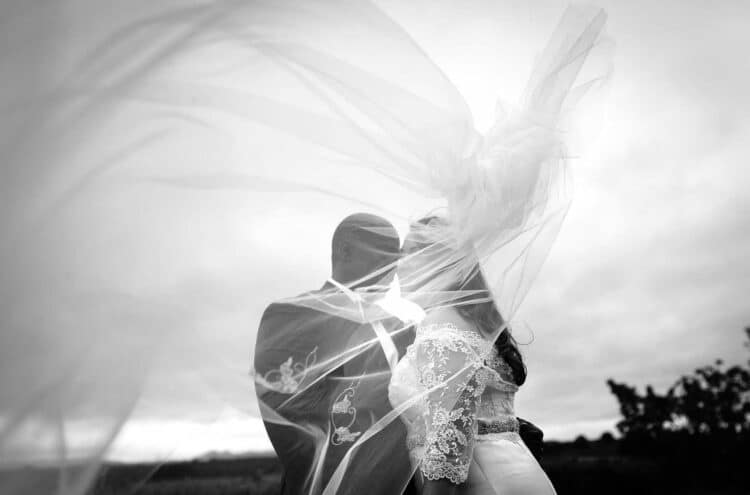 A black and white photo of a bride and groom kissing under a veil.