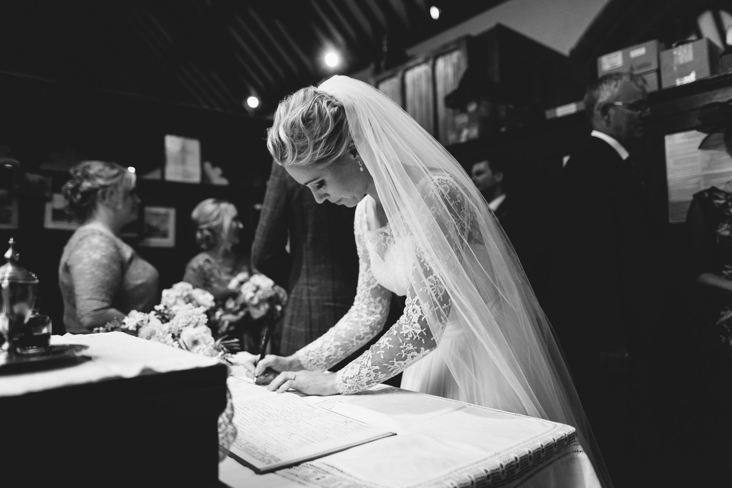 A documentary wedding photographer capturing a bride signing her wedding vows in a church.