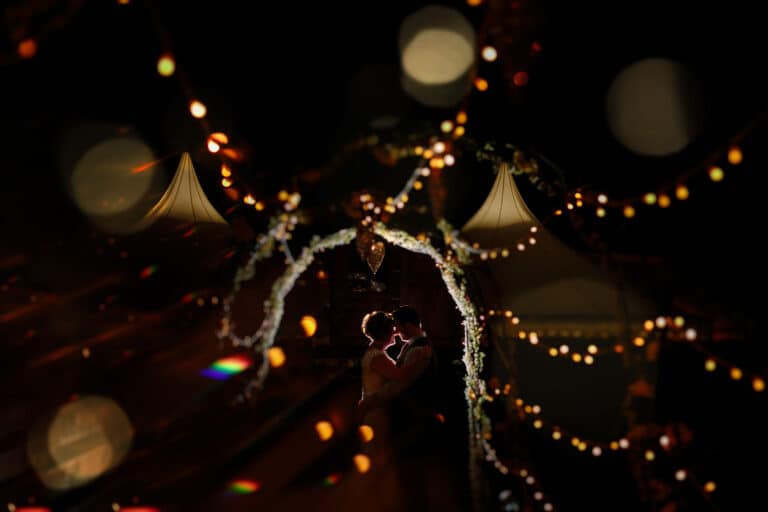Toni and Henry, a bride and groom, standing under a string of lights.