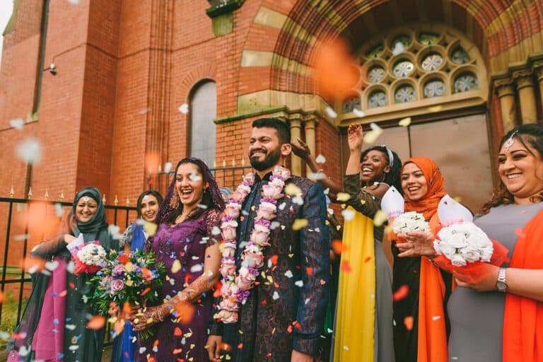 A group of Asian brides and grooms celebrating their wedding in Manchester with confetti.