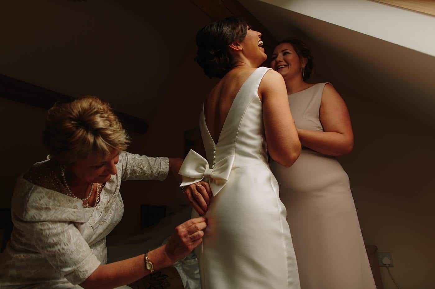 bride with her Mother and bridesmaid being fastened into her dress