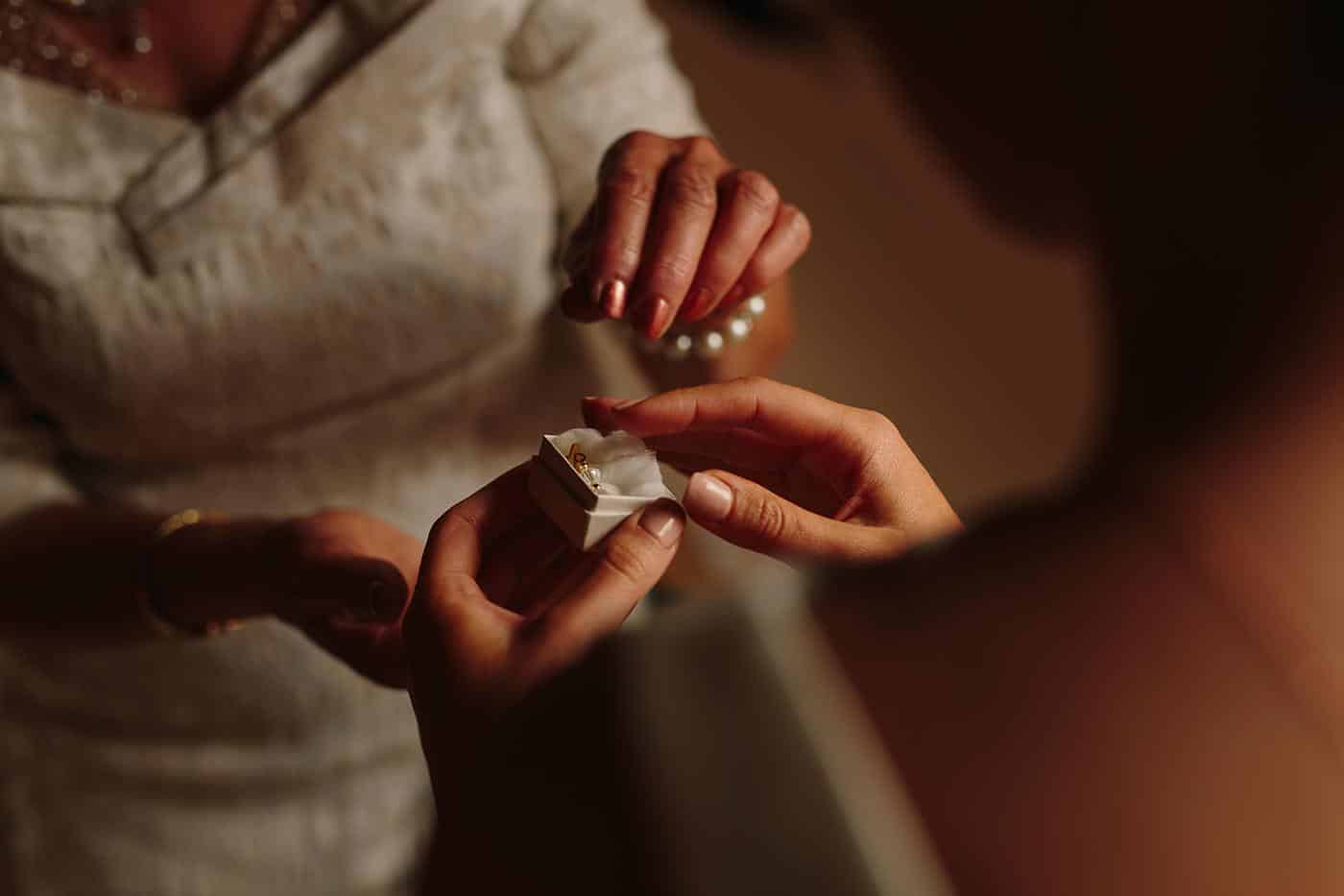 the brides mother hands her daughter a small box with earrings in