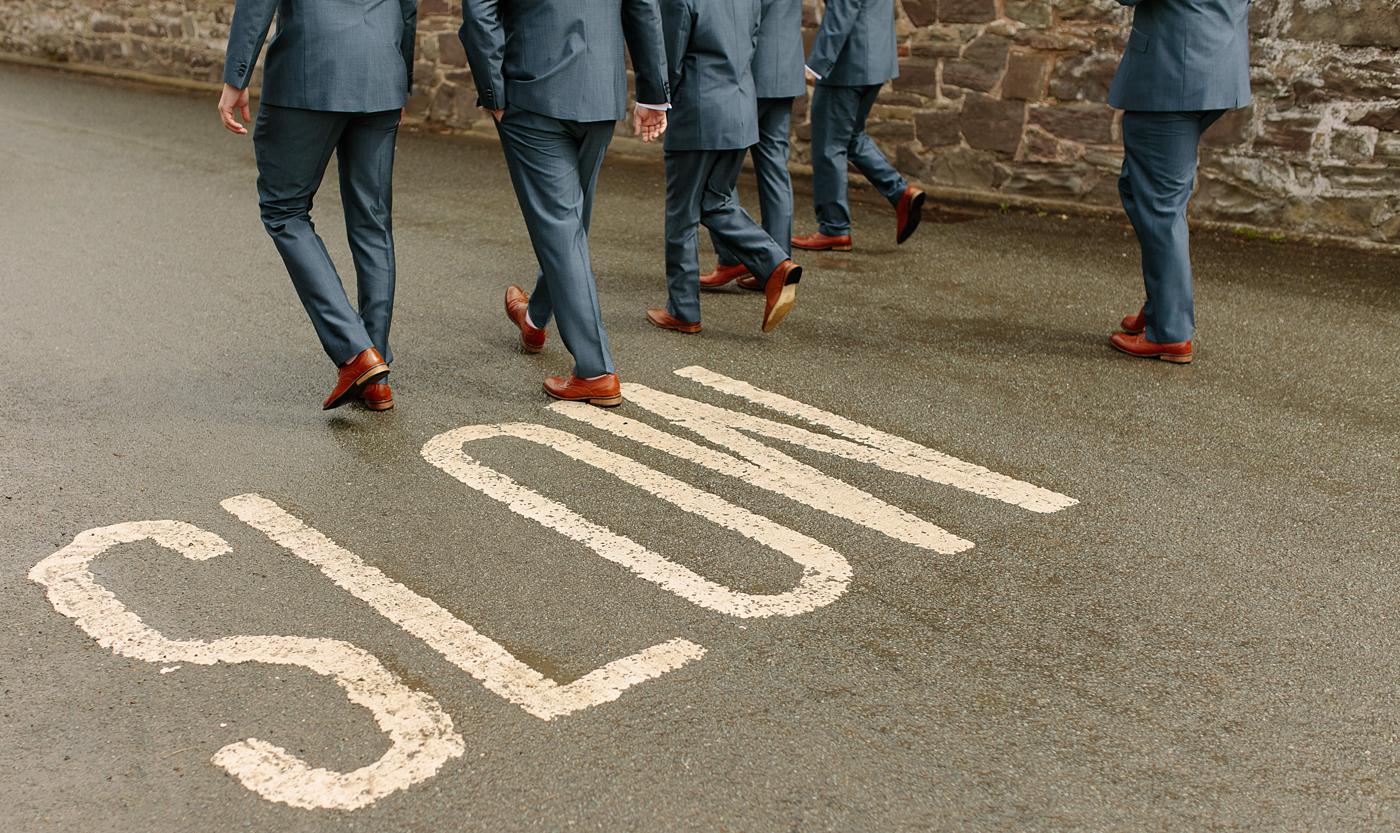 A group of men in suits walking down a street near Wistanstow Village Hall with the word slow written on it.
