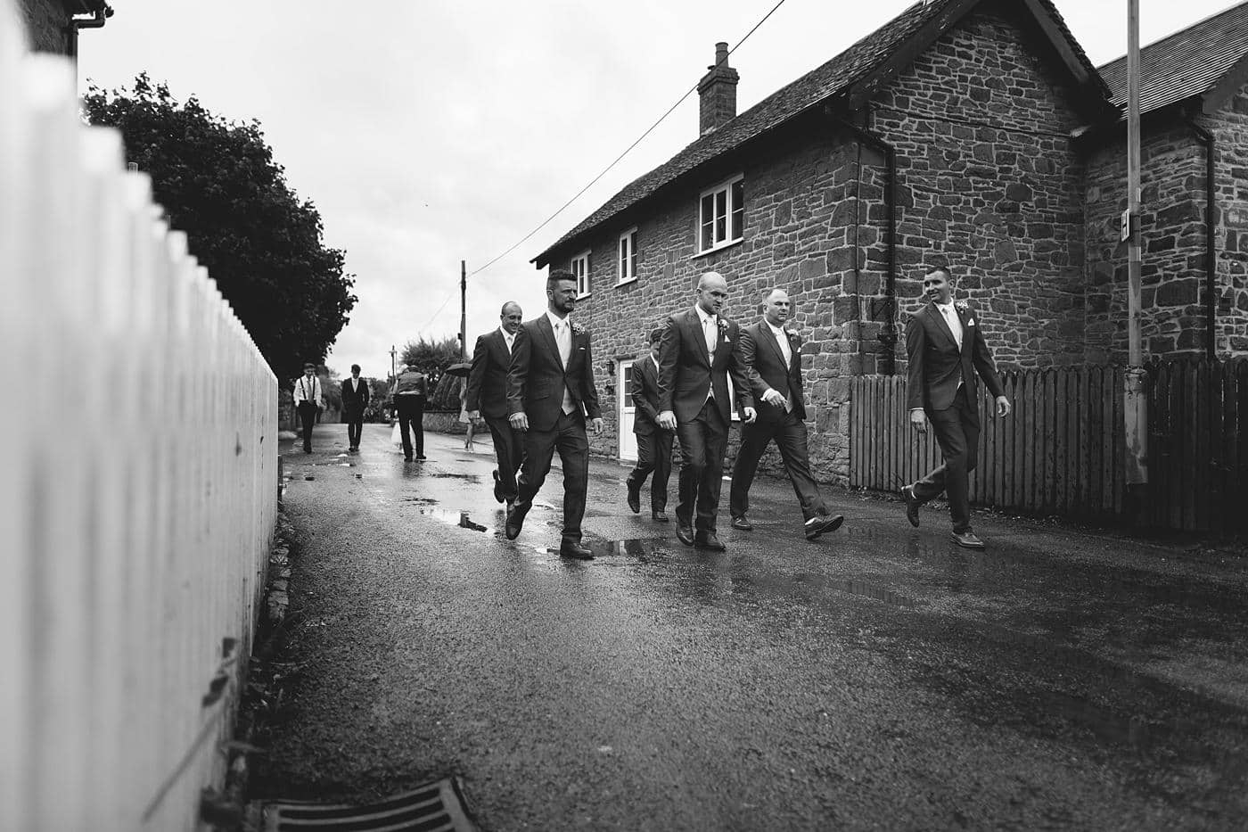 A black and white photo of groomsmen walking down a street in Wistanstow Village Hall Wedding.