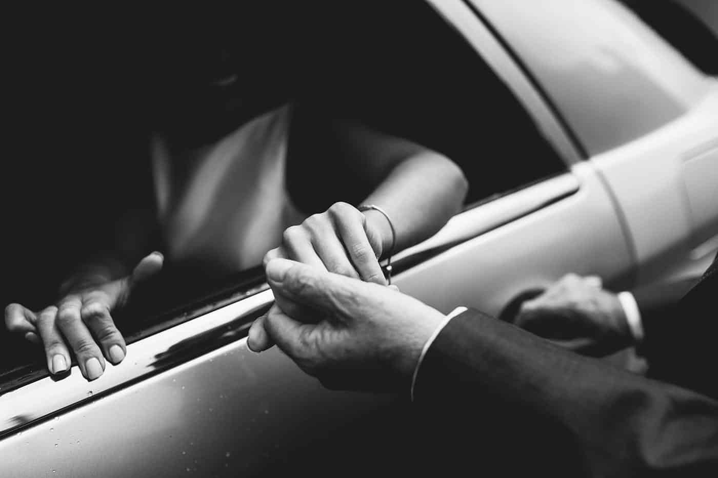 A black and white photo of a man putting his hand in the door of a limo during a wedding at Wistanstow Village Hall.
