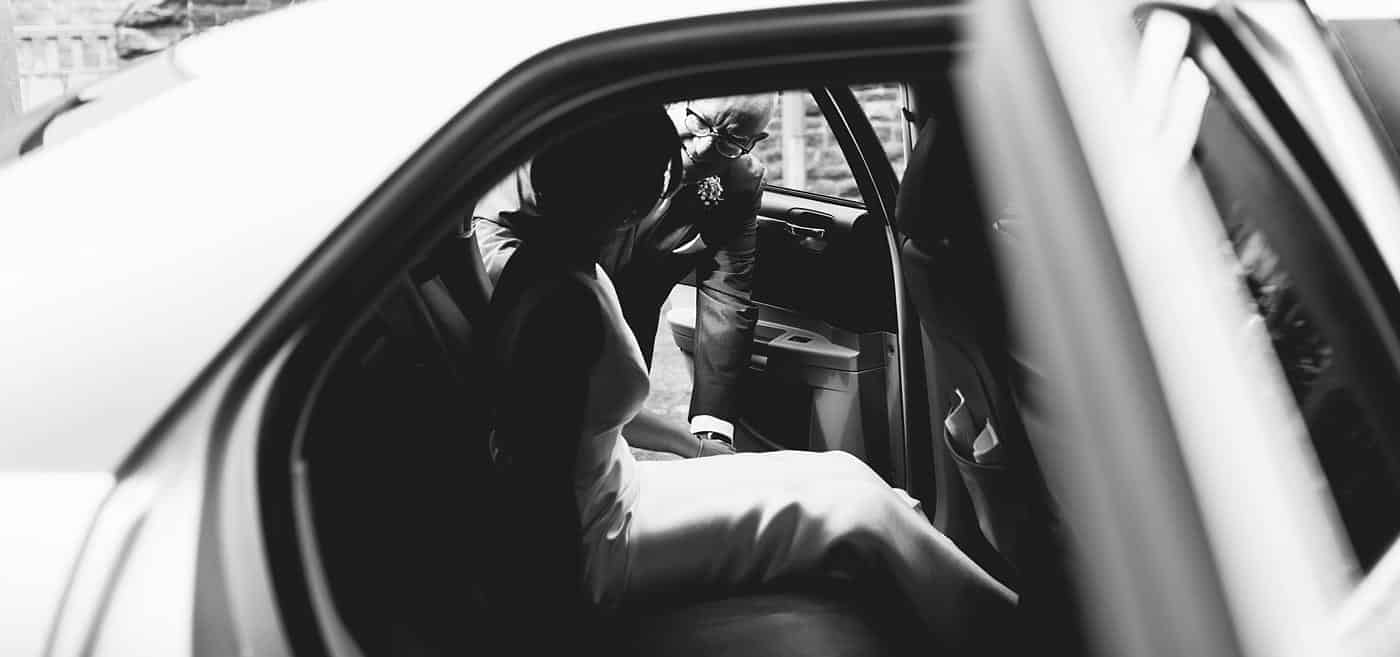 A bride and groom sitting in the back seat of a car on their wedding day at Wistanstow Village Hall.