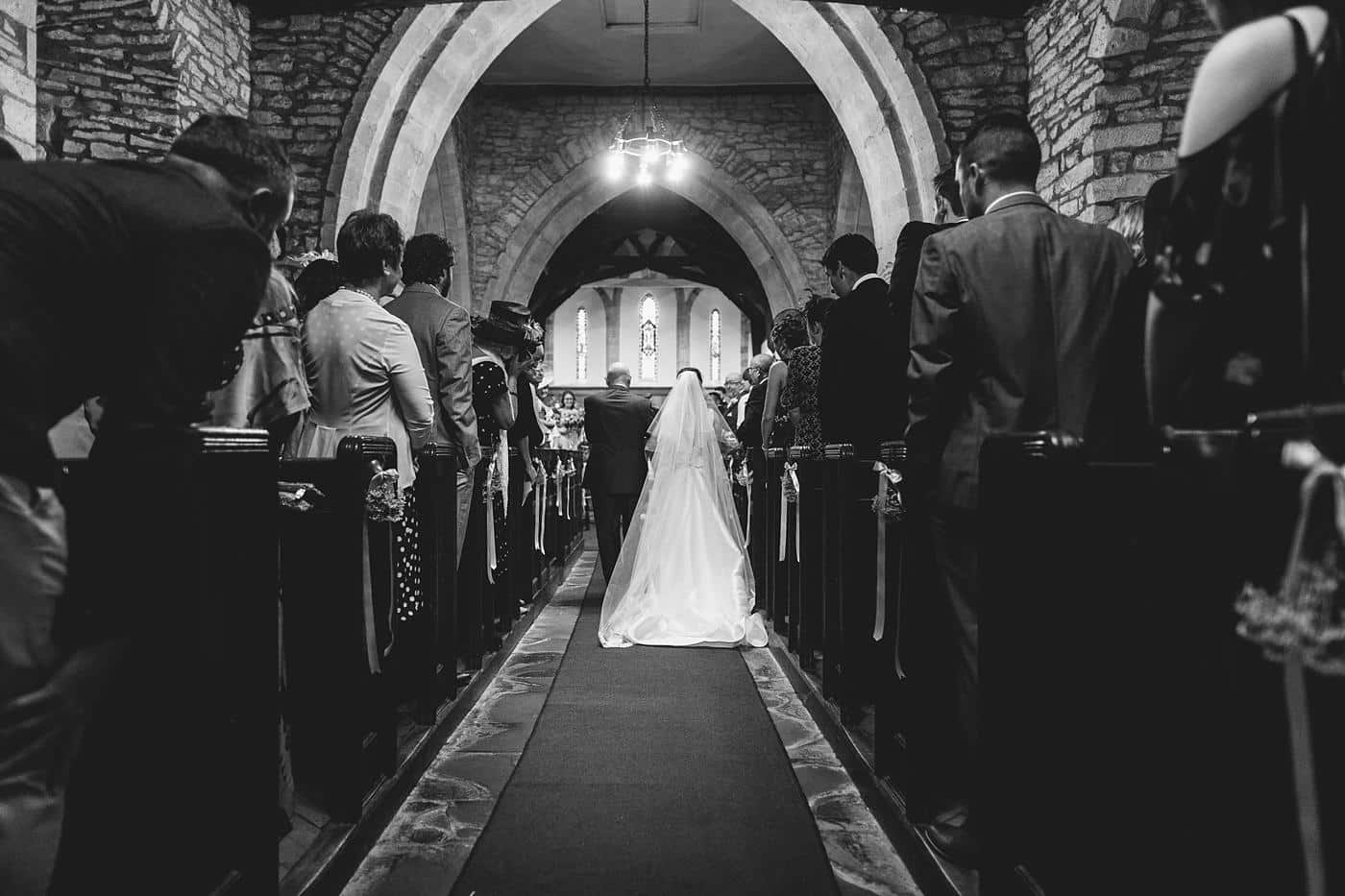 A bride walks down the aisle of Wistanstow Village Hall for her wedding ceremony.