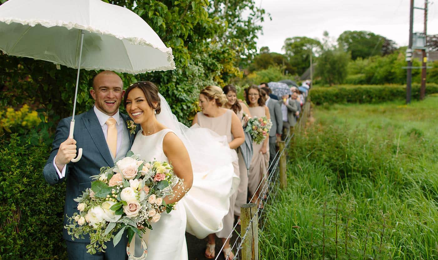A bride and groom walking down a bridge at their Wistanstow Village Hall wedding, holding an umbrella.