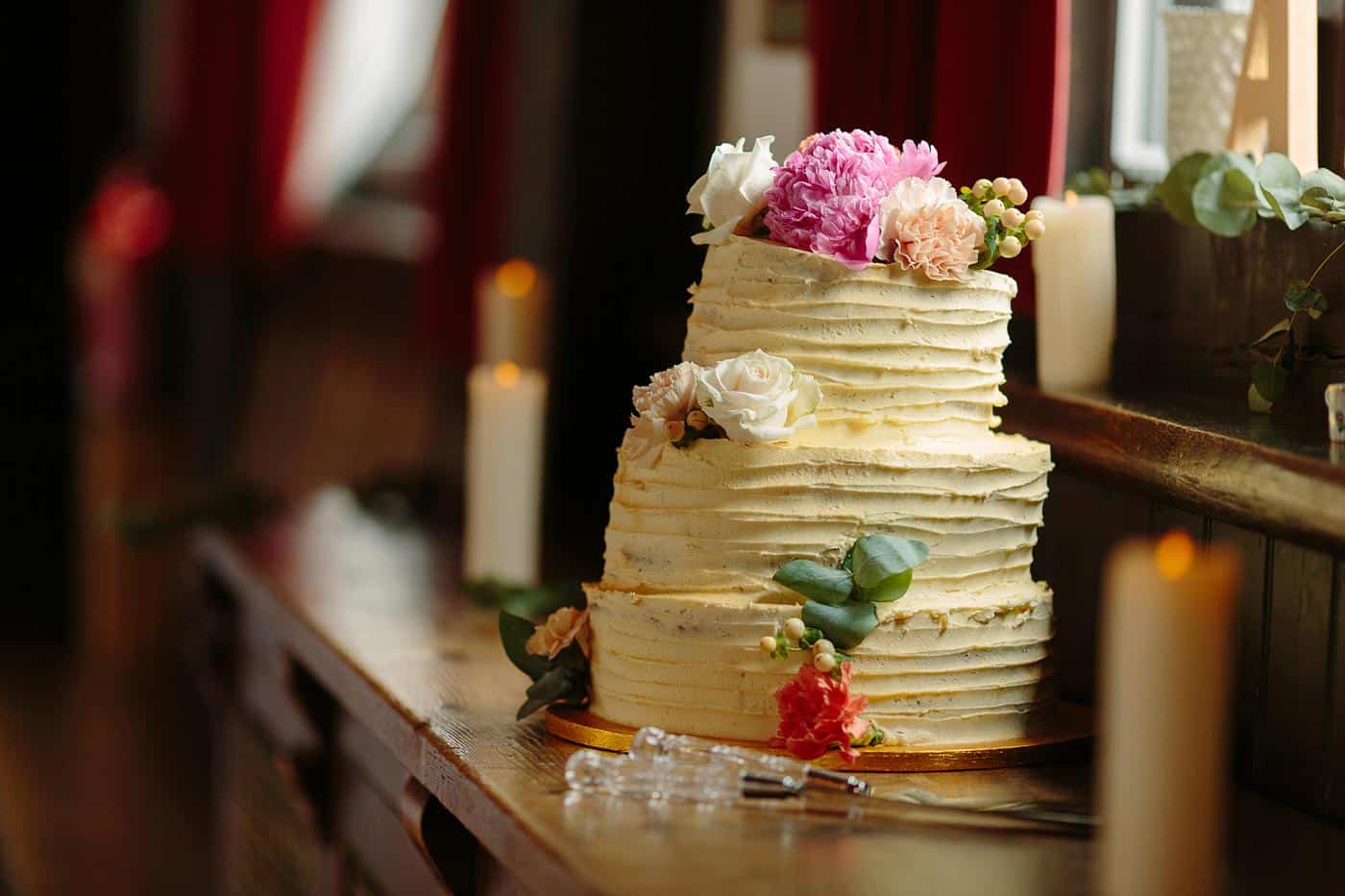 The Wistanstow Village Hall Wedding cake sits elegantly on a table, strategically placed next to a sunlit window.