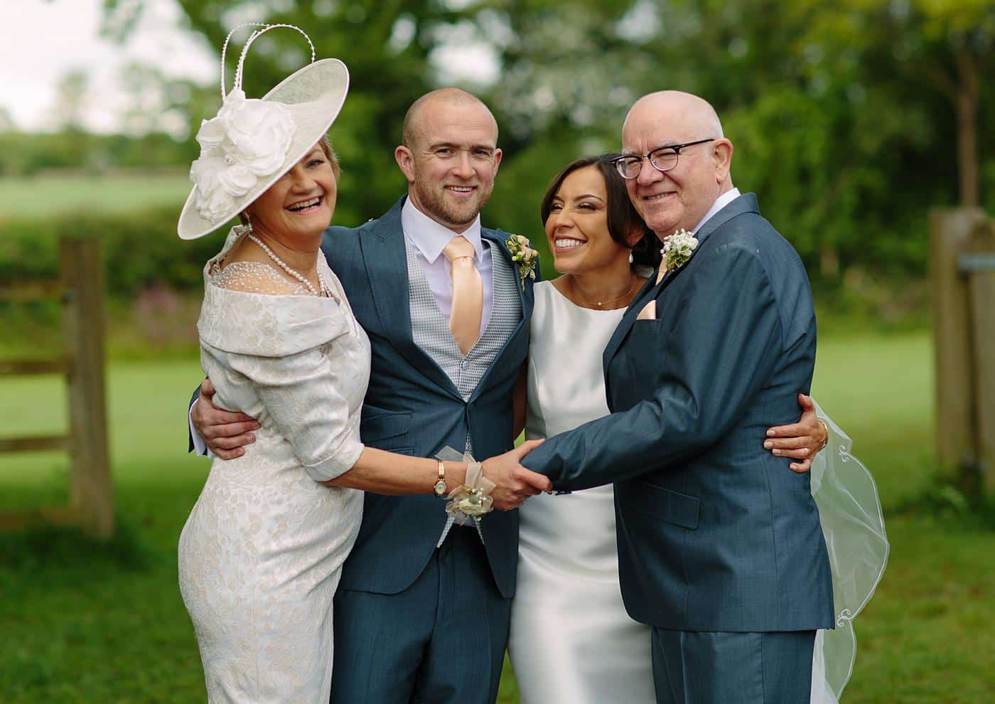 A group of people posing for a picture in front of Wistanstow Village Hall at a wedding.