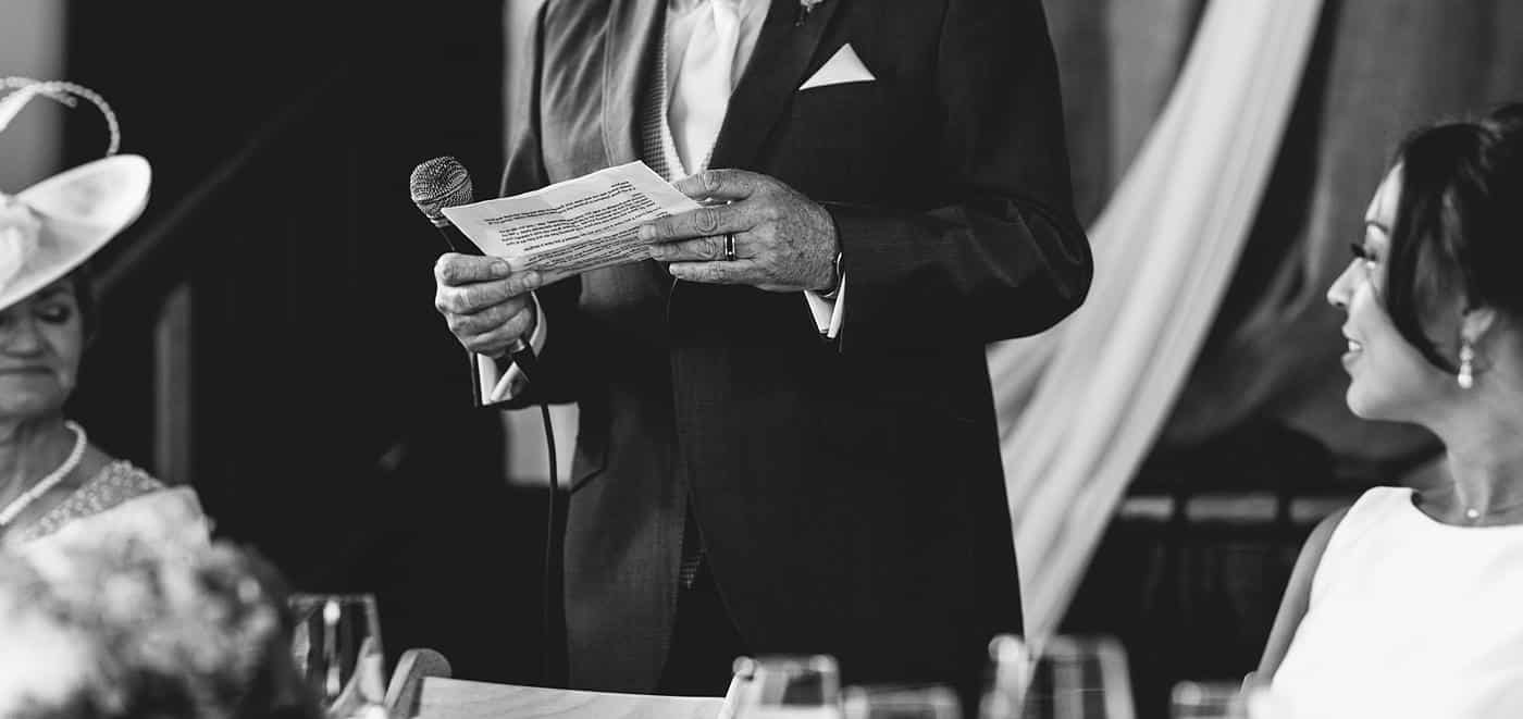 A man in a tuxedo giving a speech at a Wistanstow Village Hall wedding.