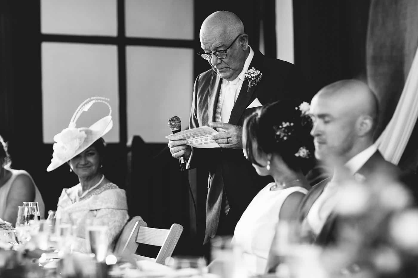 A black and white photo of a man giving a speech at a Wistanstow Village Hall wedding.