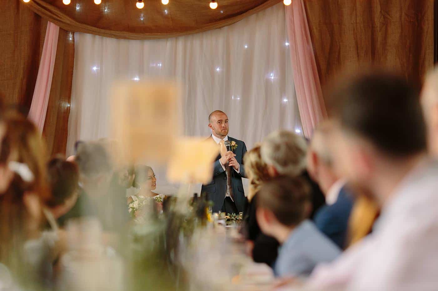 A man delivering a heartfelt speech at a wedding reception in Wistanstow Village Hall.