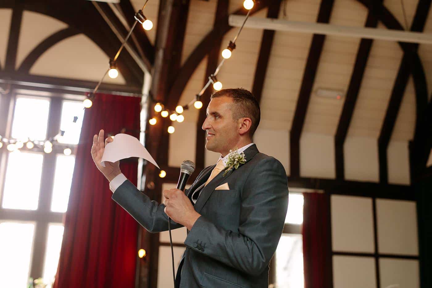 A man in a suit giving a speech into a microphone at Wistanstow Village Hall.