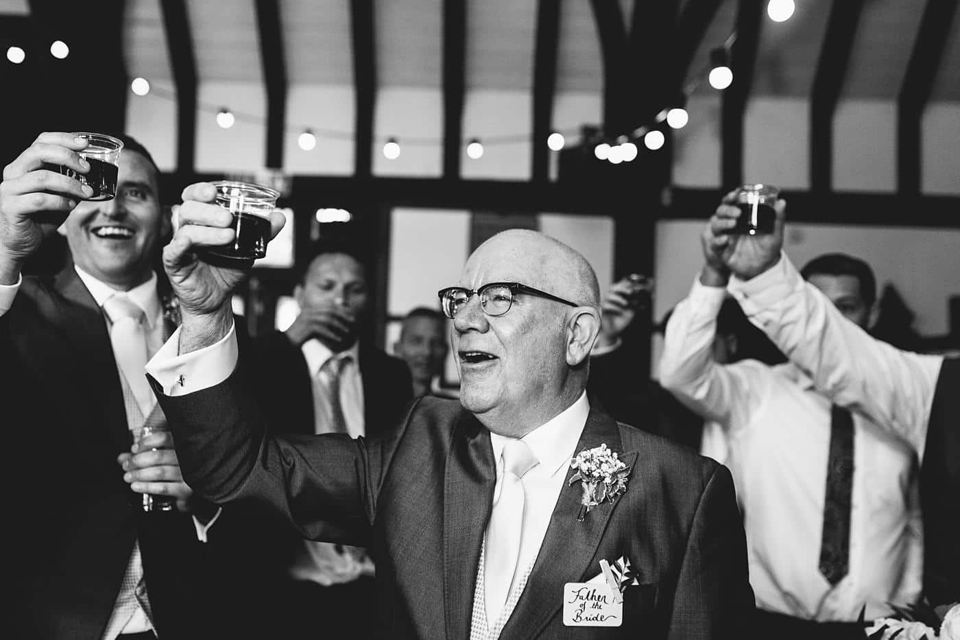 A black and white photo of a man toasting with a glass of wine at Wistanstow Village Hall Wedding.