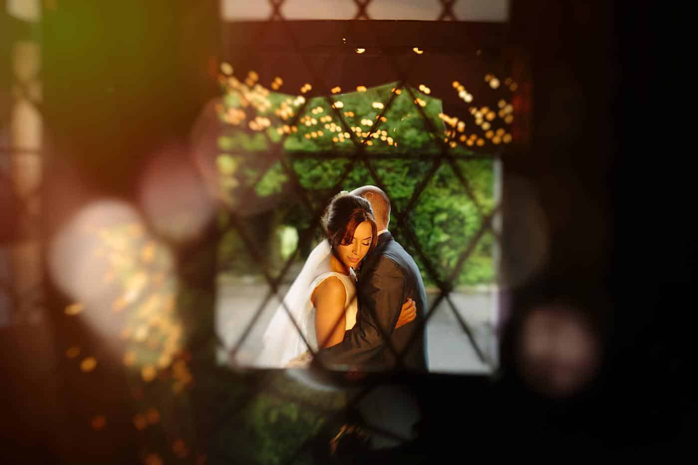 A stunning Wistanstow Village Hall wedding captures the heartfelt moment of a bride and groom embracing through a window with pure bliss.