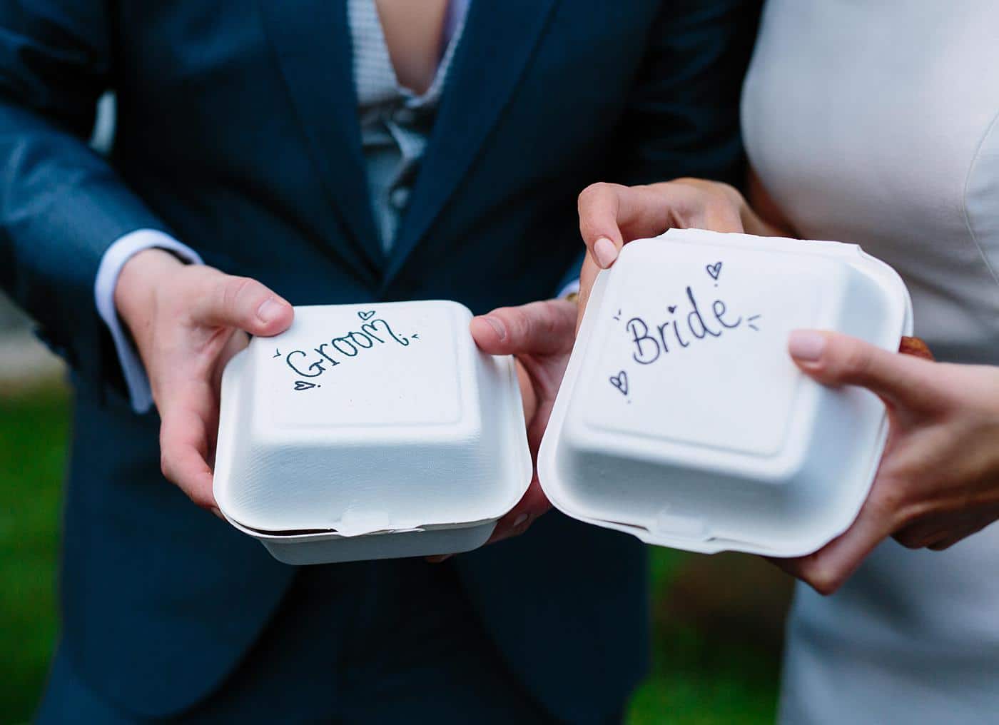 A beautiful couple, surrounded by the charming ambiance of Wistanstow Village Hall, joyfully holding two decorative boxes labeled "bride" and "groom" during their wedding celebration.