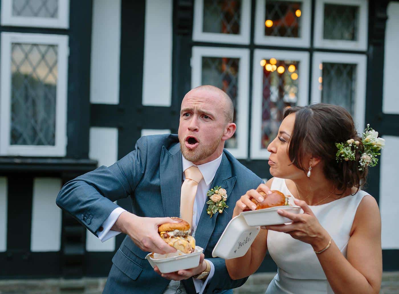 A bride and groom enjoying a hot dog in front of Wistanstow Village Hall on their wedding day.