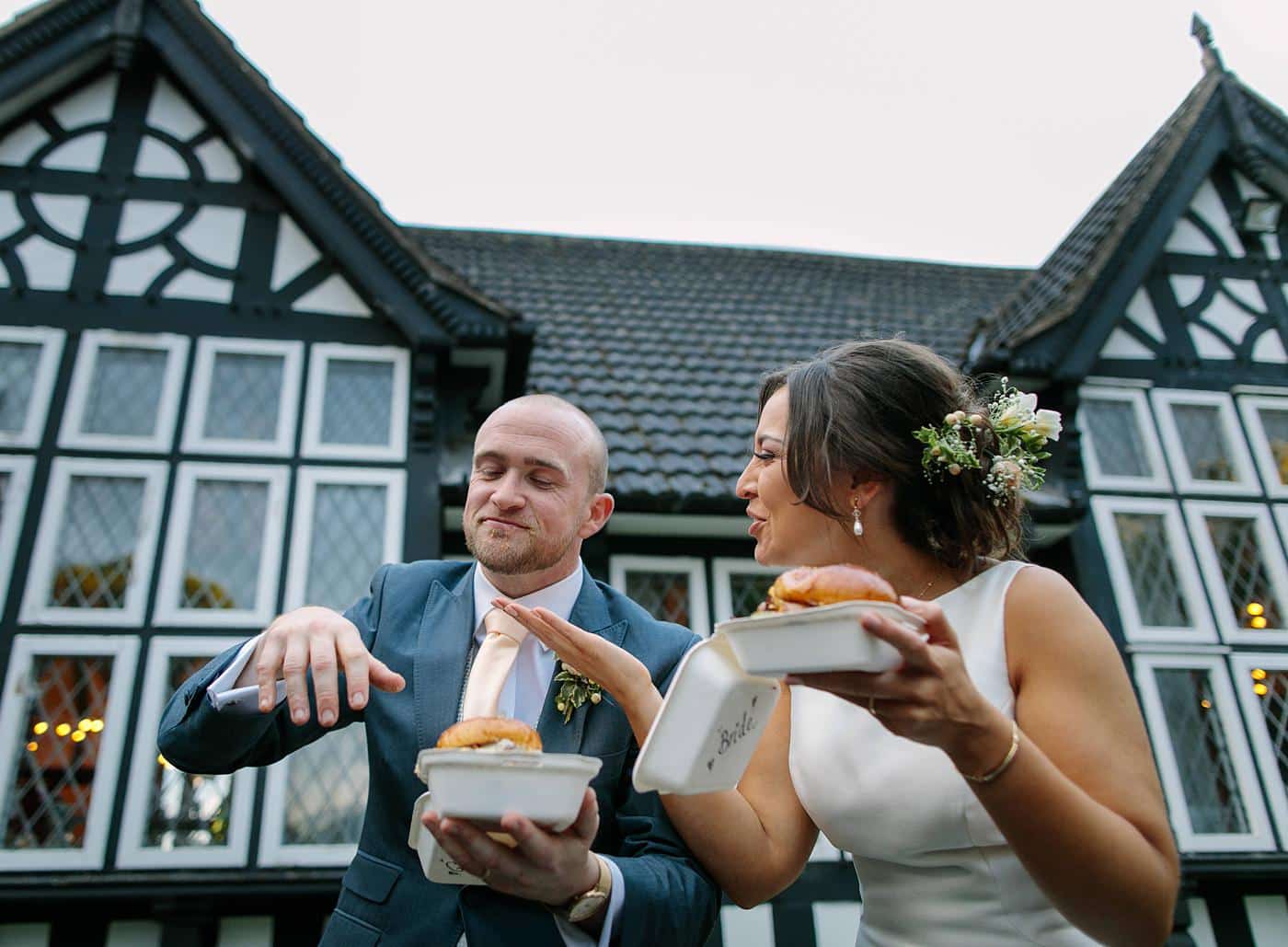 A bride and groom enjoying a donut in front of Wistanstow Village Hall on their wedding day.