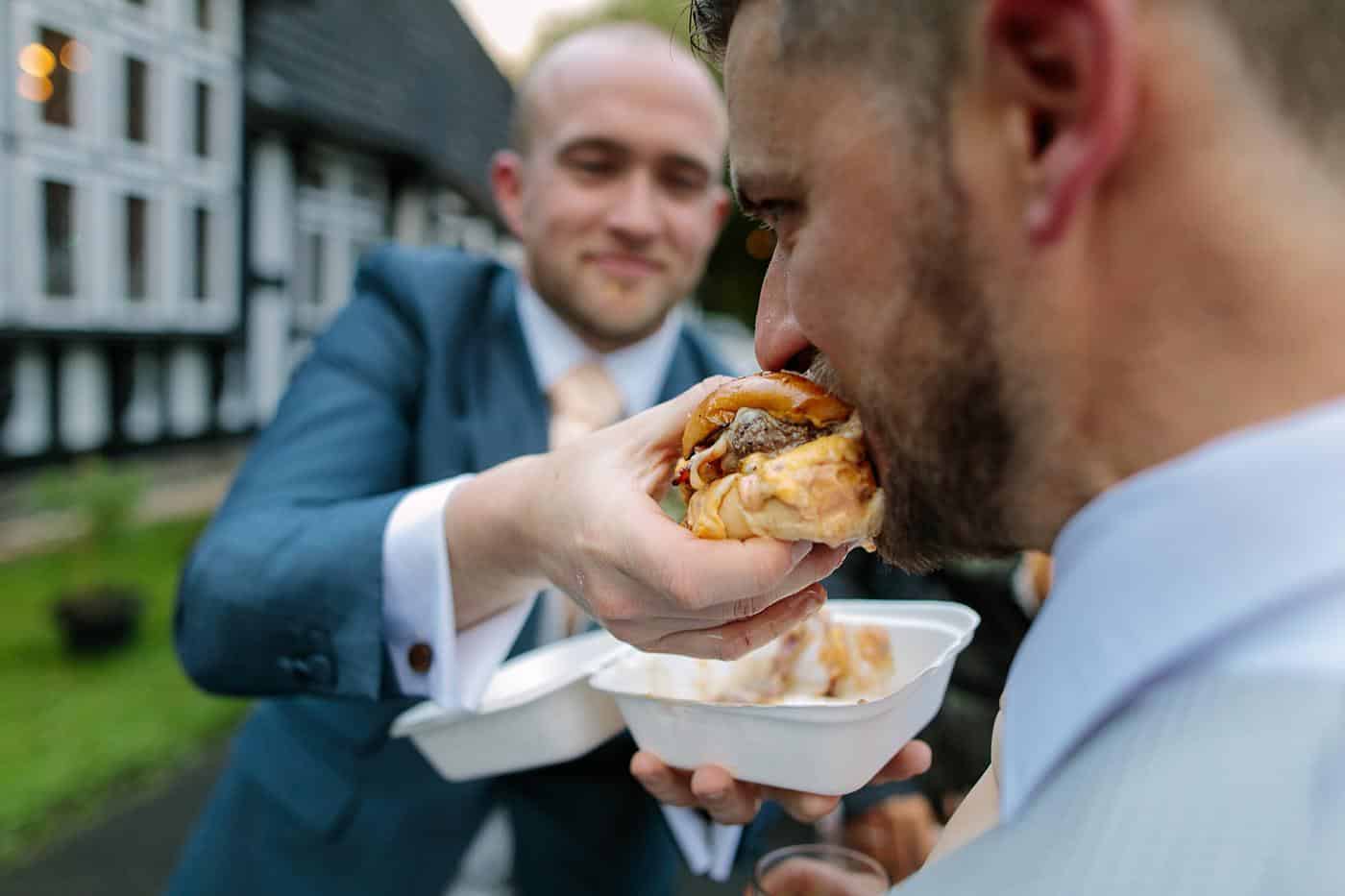 Wistanstow Village Hall Wedding attendees watch a man eating a hot dog from a plate.