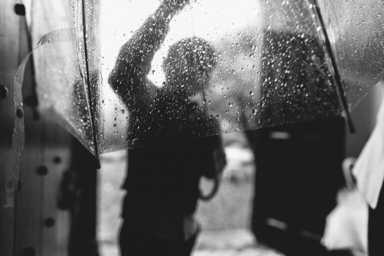 A black and white photo capturing a person holding an umbrella in the rain, evoking stories of the day.