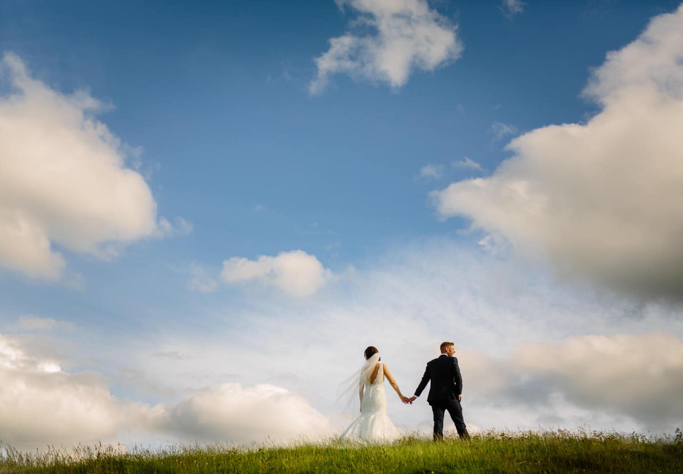 A North Wales wedding couple standing on a grassy hill under a cloudy sky.