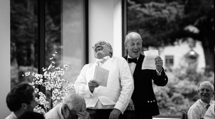 Black and white photo of two men laughing at a wedding.