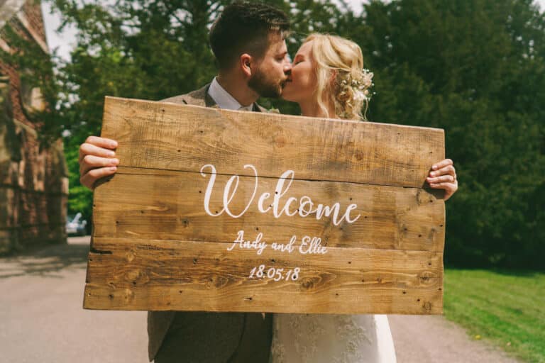 A Shropshire wedding couple sharing a kiss while holding a welcome sign.
