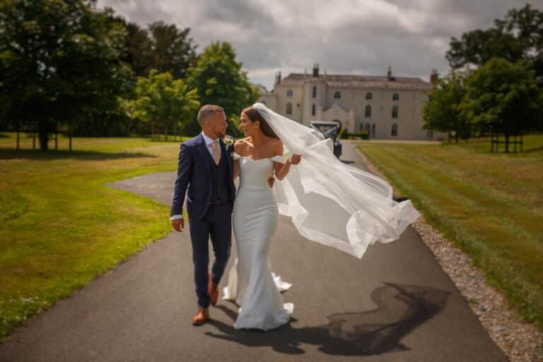 A stunning bride and groom walking down a path in front of Combermere Abbey, their dream wedding venue.