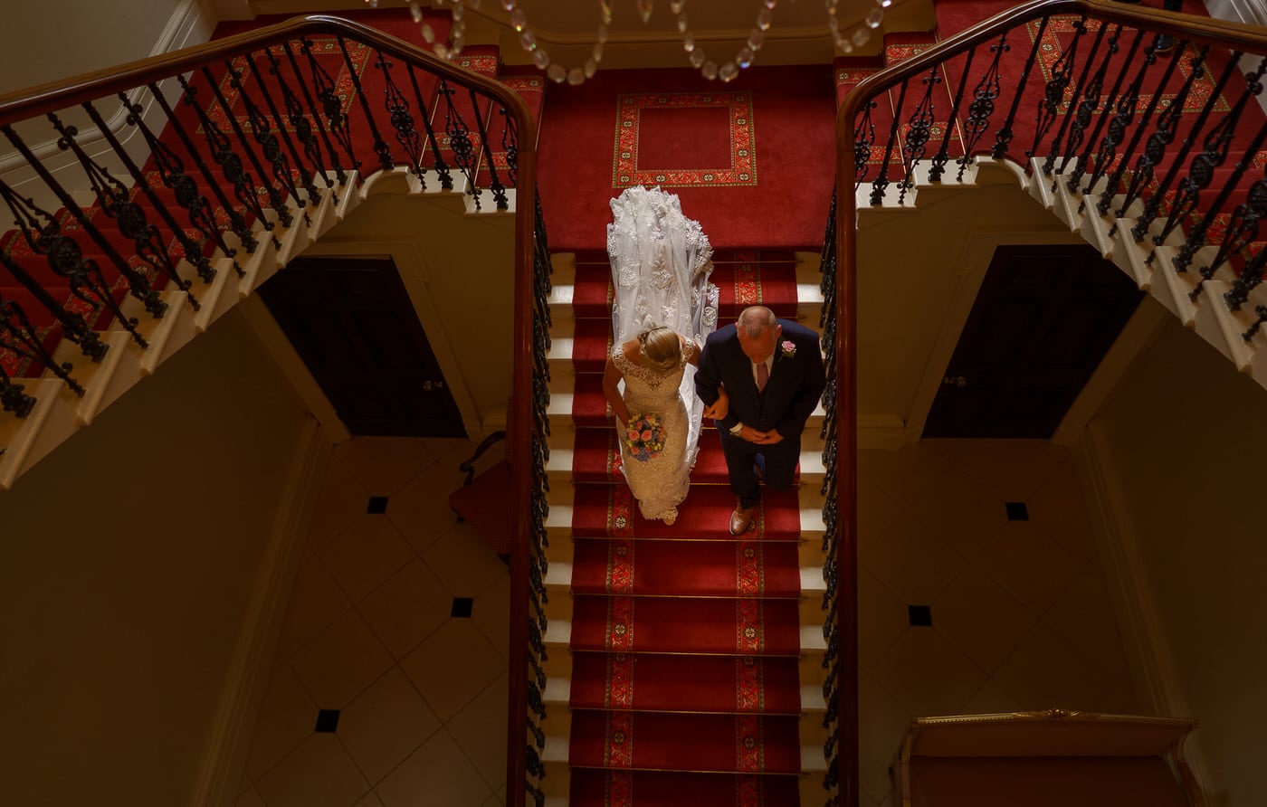 the bride and her Father descend the staircase at Netley Hall in Shropshire