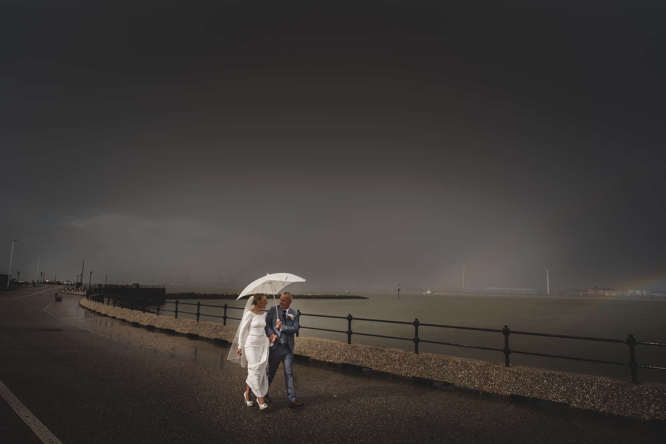 bride and groom talk a walk in the rain alongside the river Mersey, Liverpool