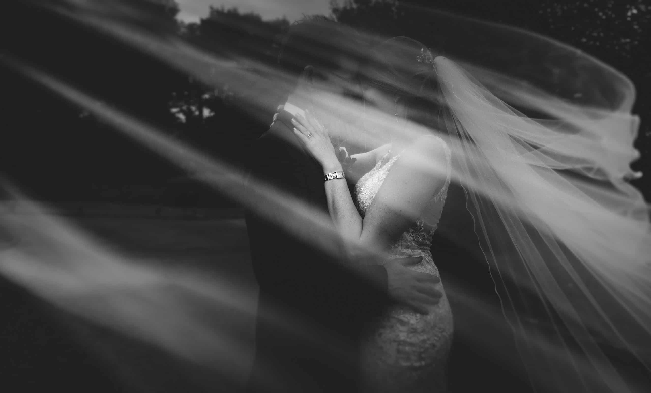 the veil of the bride wraps around the happy couple as the wind picks up