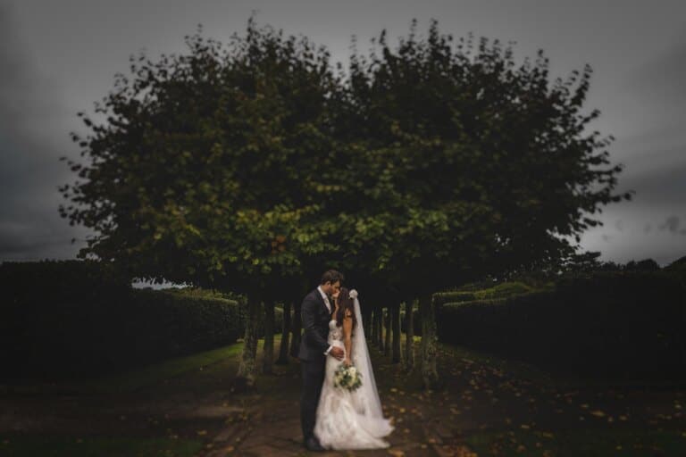 the bride and groom share a kiss in front of a heart shaped tree at Thornton Manor