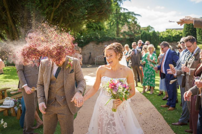 A shropshire wedding photographer captures the joyful moment of a bride and groom walking down the aisle, confetti adorning their hair.