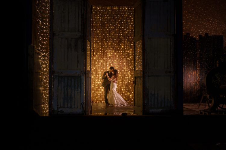 A winter bride and groom standing in front of a door with lights at Owen House Wedding Barns.