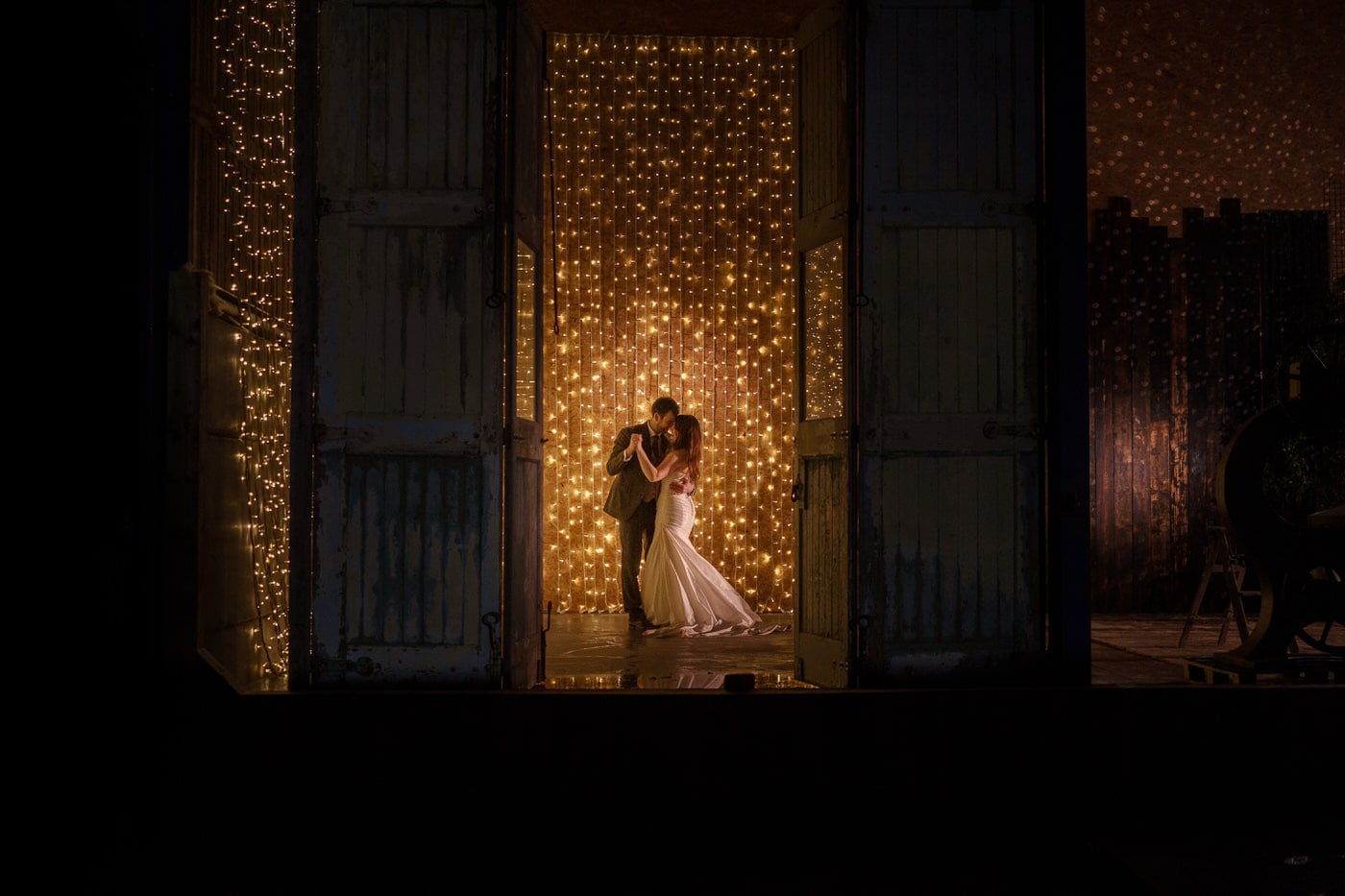 A winter bride and groom standing in front of a door with lights at Owen House Wedding Barns.