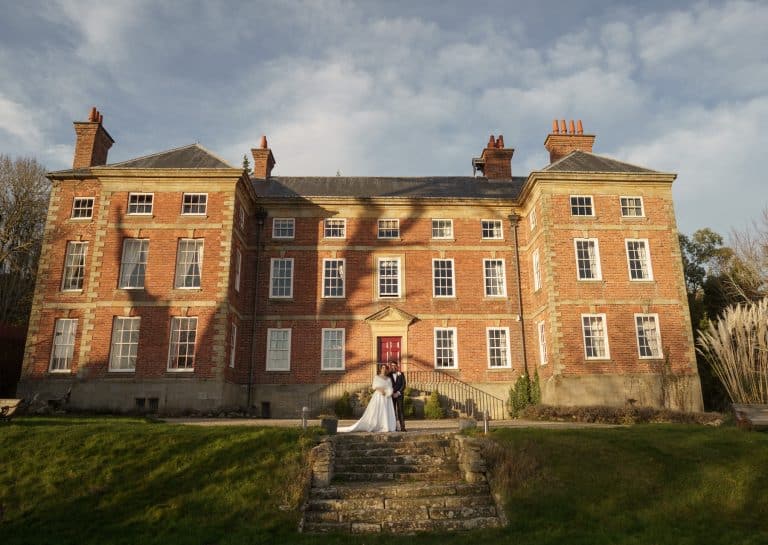 Trevor Hall Wedding - A bride and groom standing in front of a red brick mansion at Trevor Hall, Llangollen.