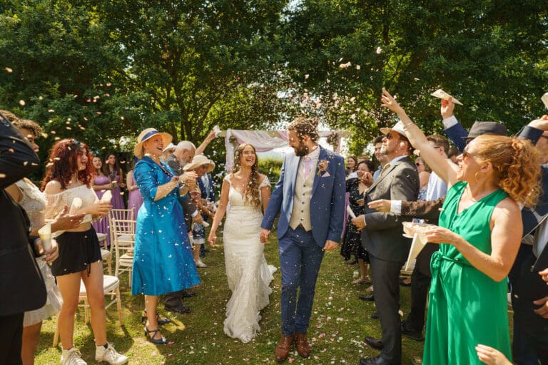 A bride and groom walk down the aisle at the Sychpwll Centre with confetti thrown at them.