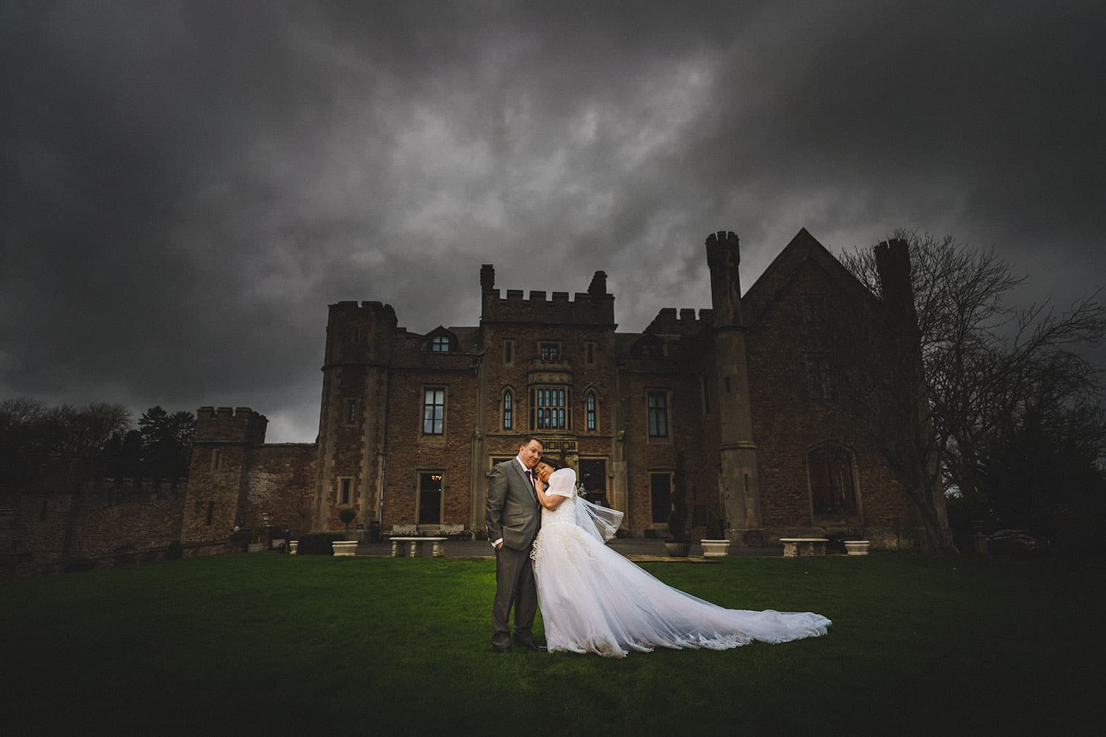 A bride and groom standing in front of Rowton Castle under a stormy sky.