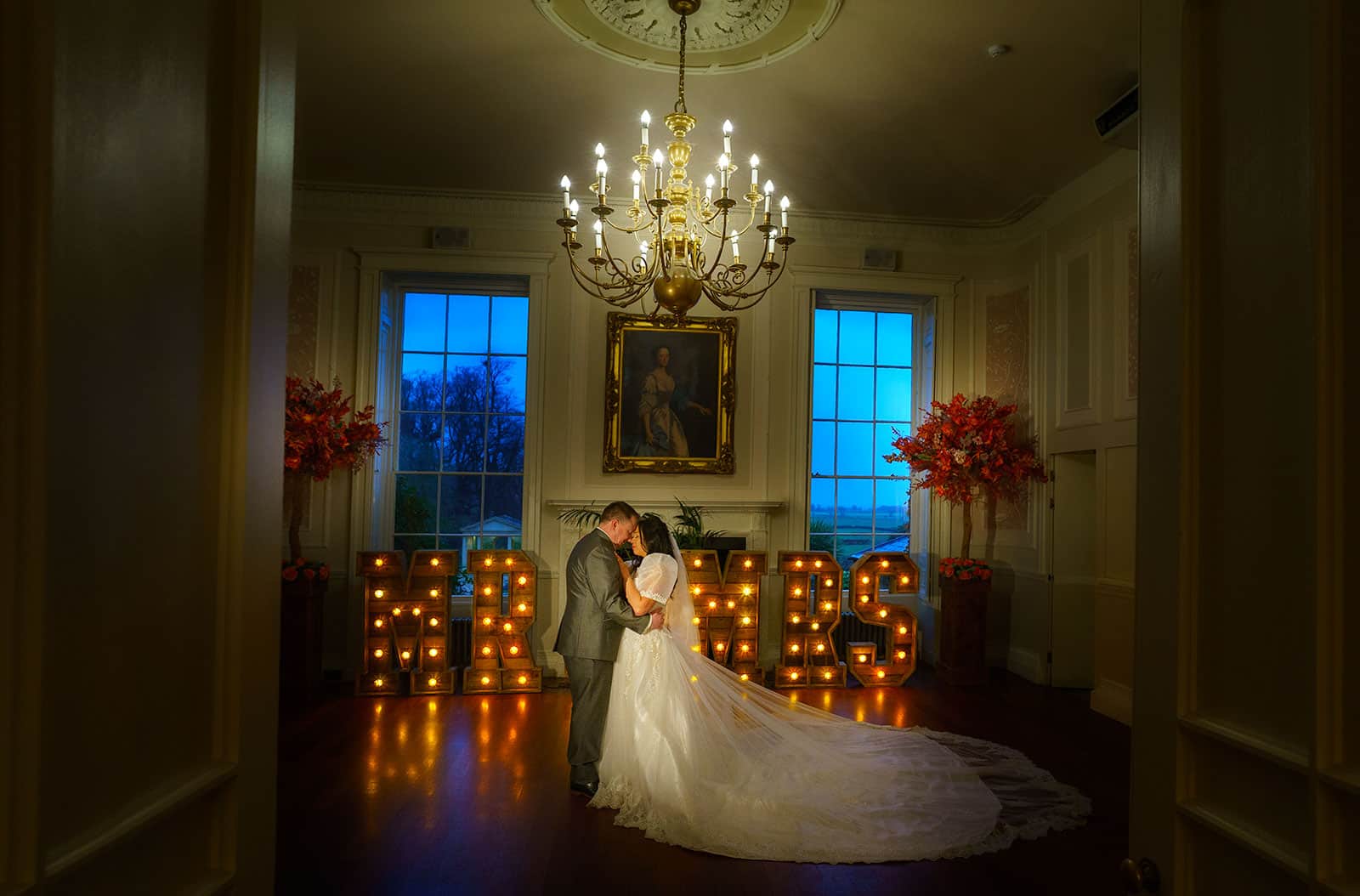 A bride and groom posing in front of a lit up welcome sign at Rowton Castle, Shrewsbury during their wedding celebration.