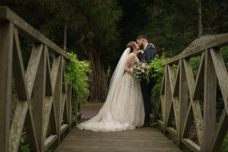 A bride and groom kiss on a wooden bridge at Tyn Dwr Hall.