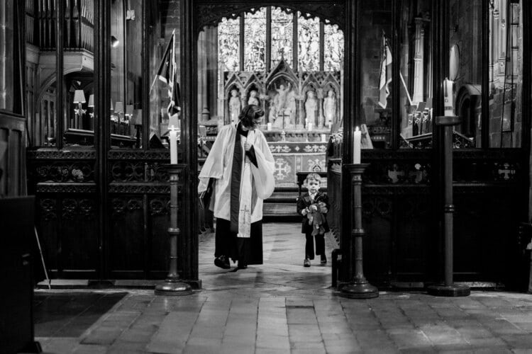 black and white image in church of vicar and young child captured by shropshire wedding photographer