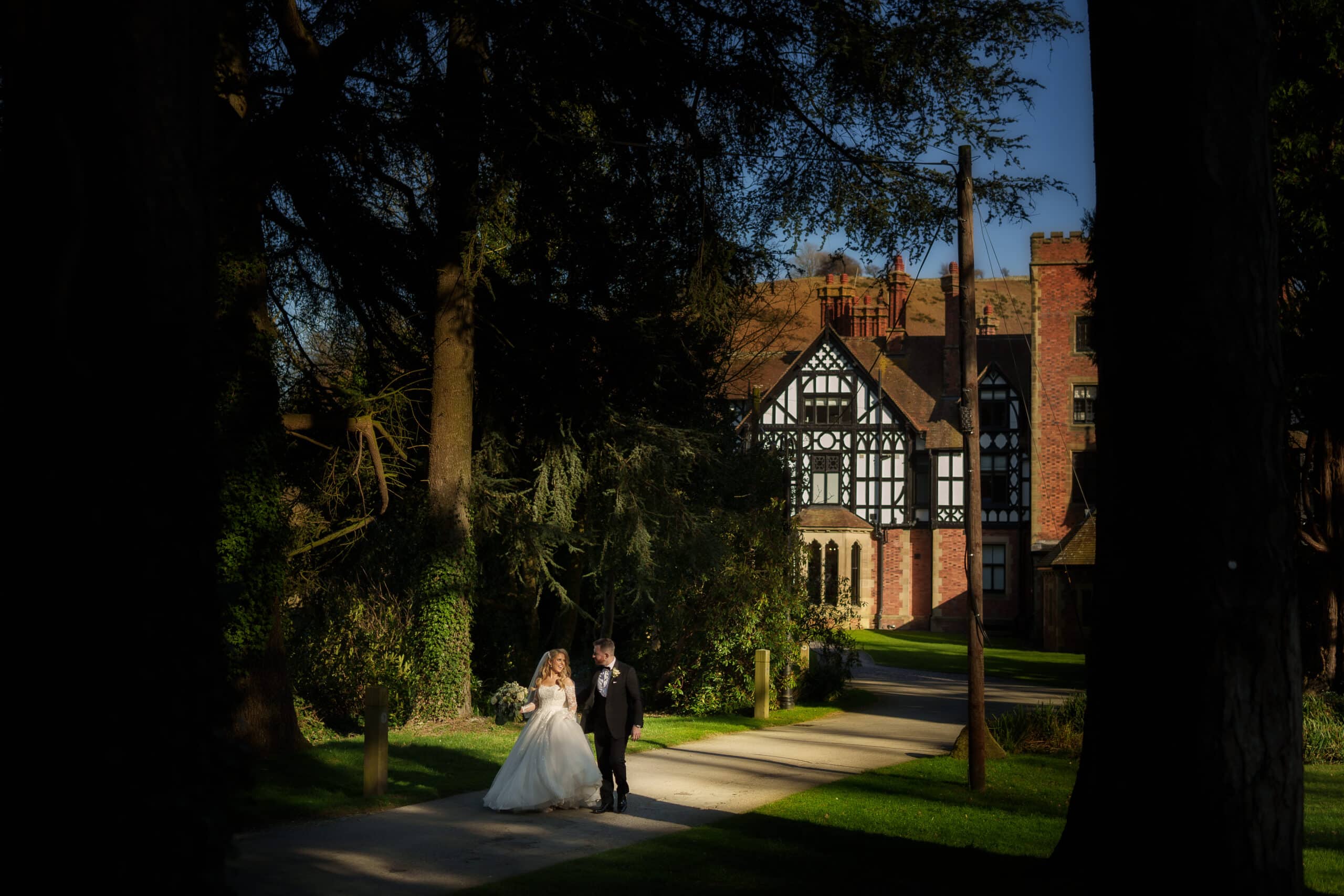A bride and groom walking down a path in front of Tyn Dwr Hall in North Wales