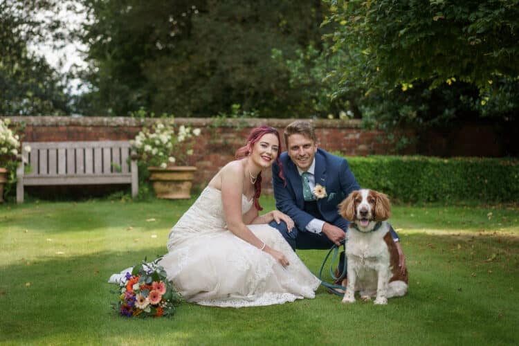 A bride and groom posing with their dog in a garden at Pimhill Barn, Shropshire's stunning wedding venue.