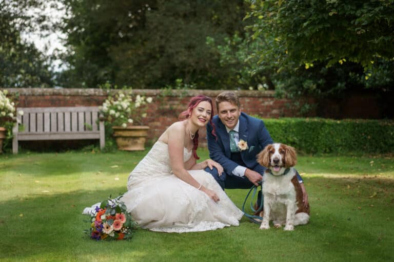 A bride and groom posing with their dog in a garden at Pimhill Barn, Shropshire's stunning wedding venue.